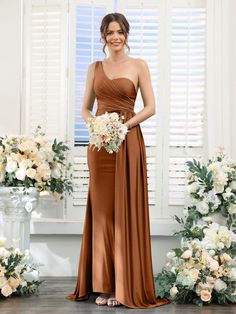 a woman standing in front of flowers wearing a brown bridesmaid dress and holding a bouquet