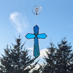 a stained glass cross hanging from the side of a window with pine trees in the background