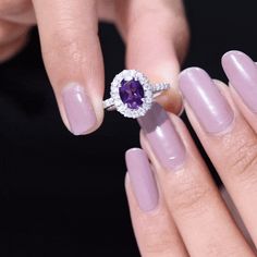 a woman's hand holding a ring with an oval shaped amethorate surrounded by diamonds