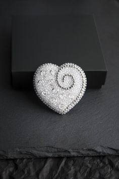 Beautiful and tender embroidered brooch in the shape of a white and silver heart. It is embroidered with seed beads, Czech crystal faceted beads and rhinestone chain. The reverse side is covered with silver faux leather. Each element of brooch is securely sewn by hand. Japanese smooth pin for a secure fit without damaging clothes.  It will decorate your look or can become an unforgettable gift for a dear person. SIZE: Length - 1.9 inches / 4.8 cm Width - 2 inches / 5.2 cm Weigh - 7 gr Will come Elegant Heart-shaped Wedding Brooch, Embellished Round Beads Jewelry Gift, Gift Jewelry With Embellished Round Beads, Embellished Jewelry With Round Beads For Gifts, Elegant Silver Heart Brooches, Elegant Silver Heart-shaped Brooches, Elegant Silver Beaded Brooches, Elegant Silver Heart Brooch, Elegant Silver Heart-shaped Brooch