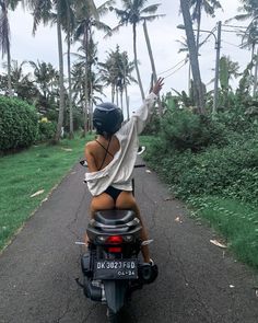 a woman riding on the back of a motorcycle down a road next to palm trees