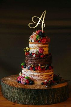 a multi layer cake with berries and flowers on top is sitting on a tree stump