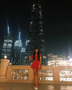 a woman standing on top of a bridge in front of a tall building at night