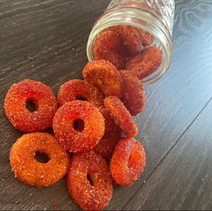 a pile of sugared donuts sitting on top of a wooden table next to a glass jar