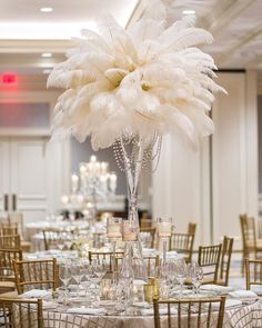 a tall centerpiece with white feathers is on top of a round table in a ballroom