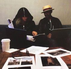 two people sitting at a table with laptops in front of them and photos on the table