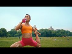 a woman drinking water from a bottle while standing in the grass with other people behind her