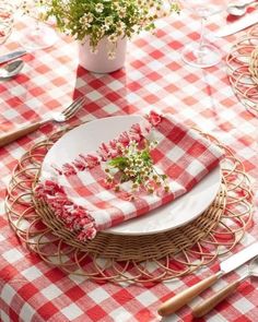 a red and white checkered table cloth with flowers on it is sitting on a wicker place setting