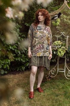 a woman with red hair standing in front of a bird cage and holding a plant