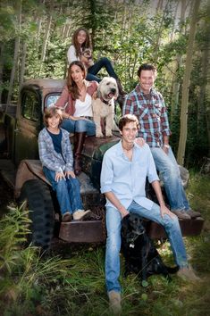 a group of people sitting on top of an old truck in the woods with a dog