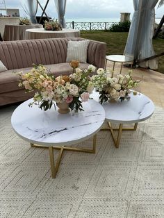 two tables with flowers on them in front of a couch