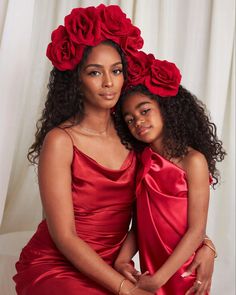 two women in red dresses hugging each other with roses on their heads and arms,