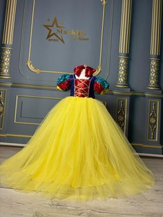 a yellow dress with red and blue on the top is displayed in front of a wall