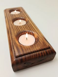 three candles are lit in a wooden holder