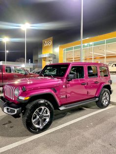 a bright pink jeep parked in front of a building at night with other vehicles behind it