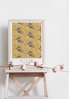 a small wooden table with cotton flowers on it and a yellow wall behind the frame