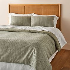 a bed with white pillows and green bedspread on top of wooden headboard