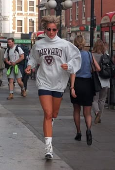 a woman is running down the street in shorts and a sweatshirt with harvard written on it