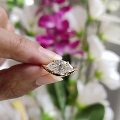 a woman's hand holding a ring with a diamond on it and flowers in the background