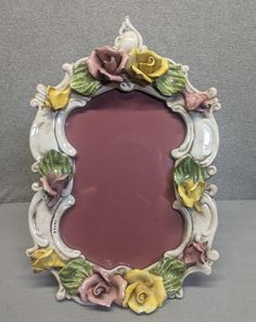 an ornately decorated mirror with flowers on it's sides and a purple background