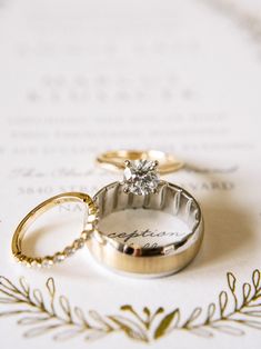 two wedding rings sitting next to each other on top of a piece of white paper