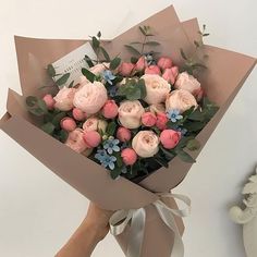 a bouquet of pink roses and blue flowers in a brown paper box with a white ribbon