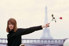 a woman holding a rose in front of the eiffel tower with her arms outstretched