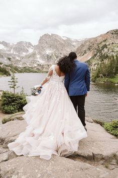 a bride and groom are standing on the edge of a cliff overlooking a mountain lake