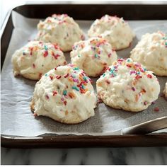 cookies with white frosting and sprinkles are on a baking sheet, ready to be eaten