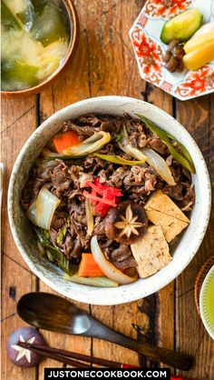 a bowl filled with beef and vegetables on top of a wooden table next to bowls of soup