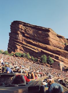 a crowd of people sitting in front of a large rock formation