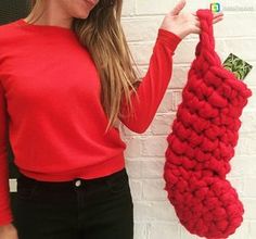 a woman holding up a red knitted christmas stocking hanging from a hook on a brick wall