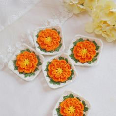 four crocheted coasters with orange flowers on them next to some yellow flowers