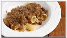 a white plate topped with pasta covered in meat and sauce on top of a wooden table