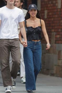 a young man and woman walking down the street holding hands, both wearing baseball caps