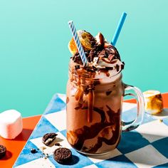 a chocolate milkshake with marshmallows, cookies and candy on a checkered tablecloth