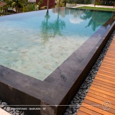 an empty swimming pool surrounded by rocks and wood flooring with trees in the background