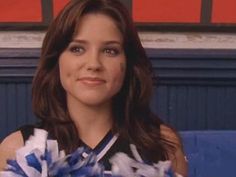 a woman in a cheerleader outfit sitting on a blue couch with her hands behind her back