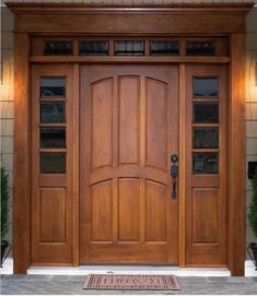 a wooden front door with glass panels on the sides and sidelights above it is an entry mat