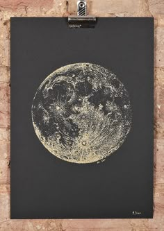 a black and gold poster with the moon on it's side hanging from a brick wall