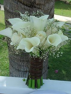 a bouquet of white flowers sitting on top of a wooden table next to a tree