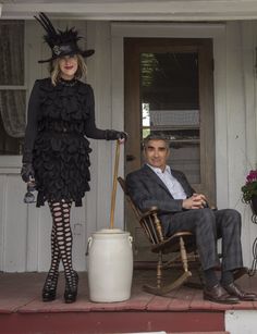 a man sitting in a rocking chair next to a woman wearing a black dress and hat