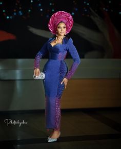 a woman in a blue dress and pink head scarf posing for the camera with her hand on her hip