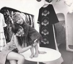 two women and a child are sitting on a table in front of a rack of shirts