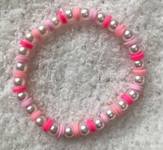 a pink and silver beaded bracelet with pearls on it's end is laying on a white carpet