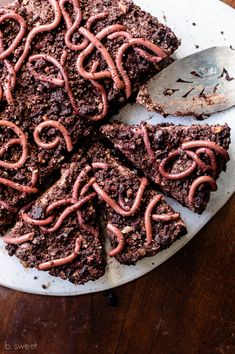 chocolate brownies with red icing are on a white platter next to a spoon