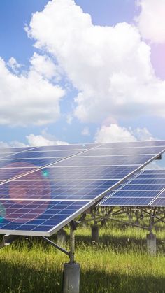 two solar panels in the grass under a cloudy blue sky with sun shining on them