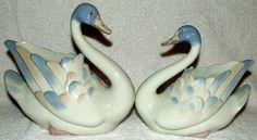 two ceramic swans sitting on top of a white cloth covered table next to each other