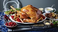 a roasted turkey on a platter with cranberries and other holiday foods around it