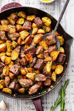 a skillet filled with potatoes and herbs next to some seasoning on the side